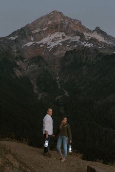 a man and woman standing on top of a mountain at night with their hands in each others'pockets