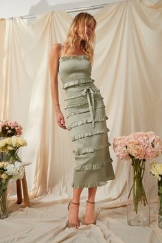 a woman standing in front of flowers wearing a dress with ruffles on it