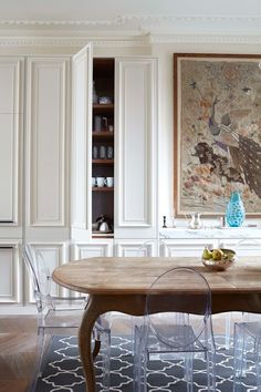 a dining room table with clear chairs and an art piece on the wall behind it