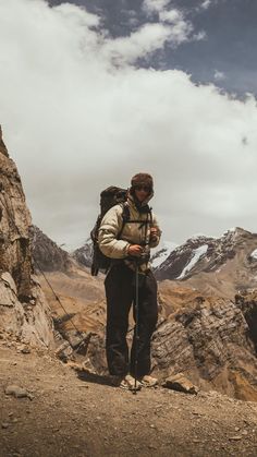 a man standing on top of a mountain with a backpack and hiking poles in his hands