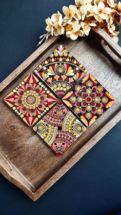 a wooden tray with decorative designs on it and some flowers in the corner next to it