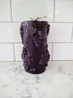 a candle with grapes on it sitting on a marble counter next to a white tile wall