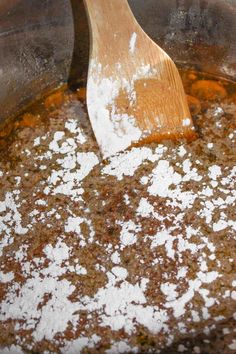 a wooden spatula is stirring some food in a pot with brown and white stuff