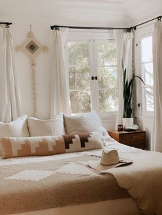 a bed with pillows and blankets on top of it in front of two large windows