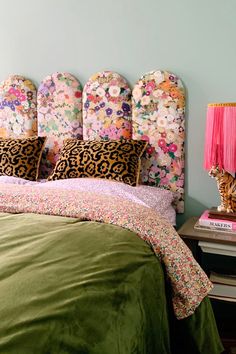 a green bed with floral headboard and pink lamps on nightstands next to it