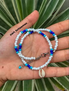 a hand holding a blue and white beaded bracelet with a seashell charm on it