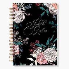 a black notebook with pink and white flowers on the front, surrounded by greenery