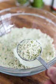 a spoon in a glass bowl filled with white sauce on top of a wooden table