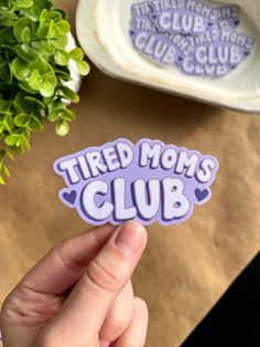 a person holding up a sticker that says tired mom's club on it