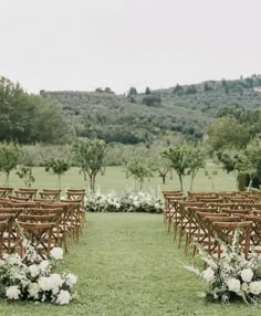 an outdoor ceremony setup with wooden chairs and white flowers on the grass in front of trees