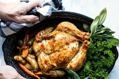 two hands holding a roasting pan filled with chicken and vegetables