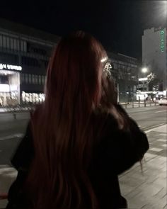 a woman with long red hair walking down the street at night