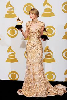 the woman is holding two awards in her hand and wearing a gold dress with sequins on it