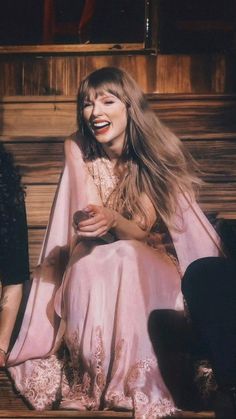 a woman in a pink dress sitting on a wooden bench with her hair blowing back