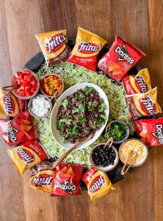 a platter filled with taco salad, chips and dips on top of a wooden table