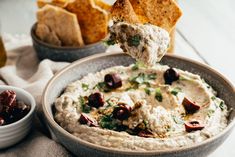 a bowl filled with hummus, olives and pita chips next to some dipping sauce