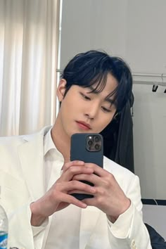 a man taking a selfie with his cell phone in front of him and wearing a white suit