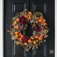 a wreath on the front door with flowers and leaves hanging from it's sides