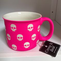 a pink mug with white skulls on it next to a black and white tag that says cool & cozy