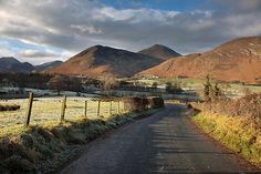 a rural road with mountains in the background and frosty grass on the ground,