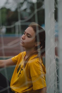 a girl in a yellow shirt leaning against a soccer goal net with her hand on the ball