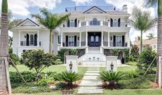 a large white house with palm trees in the front yard and stairs leading up to it