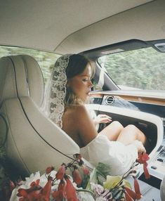 a woman sitting in the back seat of a car wearing a wedding dress and veil