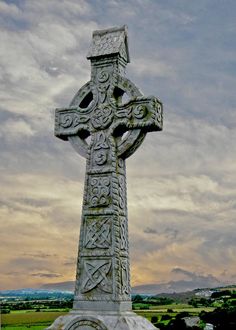 a large stone cross sitting on top of a lush green field under a cloudy sky