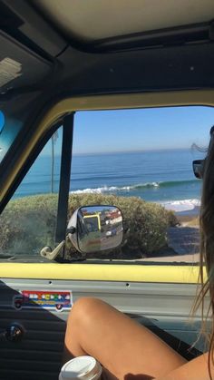 a woman sitting in the back seat of a truck looking out at the ocean and beach