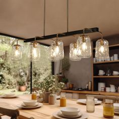 a wooden table topped with lots of plates and glasses next to a light fixture hanging from the ceiling