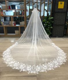 a white wedding veil with flowers on the bottom is hanging in front of a bookshelf