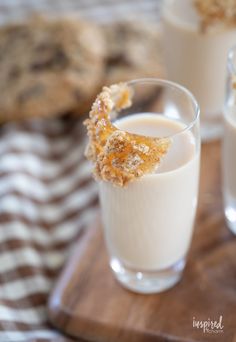 two glasses filled with milk sitting on top of a wooden cutting board next to cookies