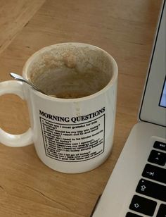 a cup of coffee sitting next to a laptop on a wooden table with a spoon in it