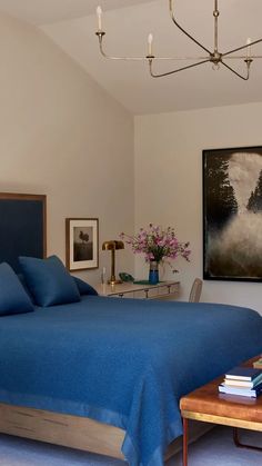 a bed with blue sheets and pillows in a bedroom next to a painting on the wall