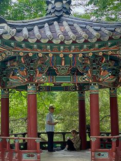 a man standing in front of a red and green gazebo with people sitting under it