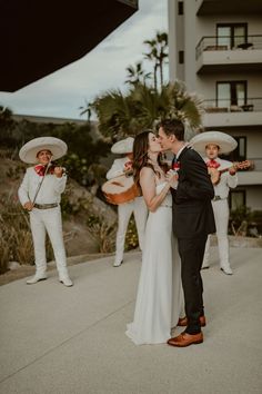 a bride and groom kissing in front of some mexican musicians