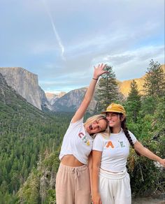 two women standing on top of a mountain with their arms in the air and smiling