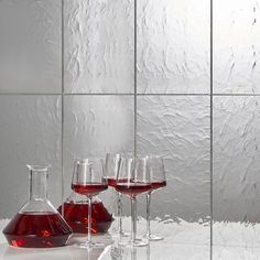 three wine glasses with red liquid in them sitting on a counter top next to a decanter