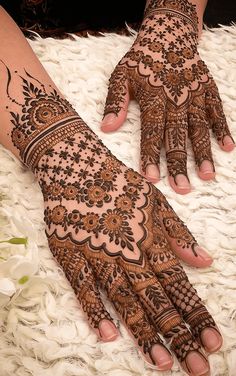 two hands with henna tattoos on them sitting on a white rug next to flowers