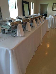 the buffet table is set up with white linens and silver trays on each side