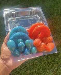 a person holding up a plastic container filled with oranges and blue gummy bears