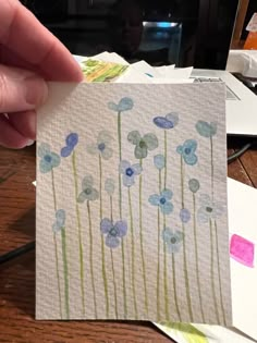 a person holding up a piece of paper with watercolor flowers on it