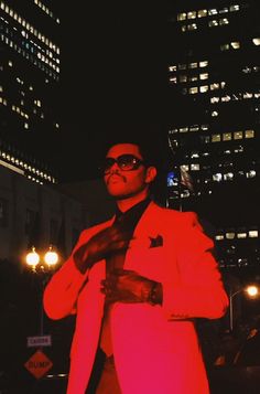 a man in a red suit and sunglasses standing outside at night with his hands on his chest