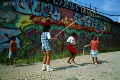 three children playing baseball in front of a graffiti covered wall