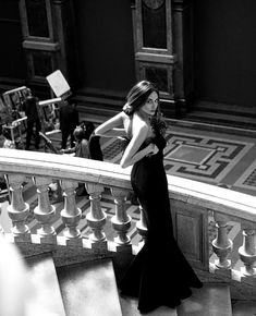 a woman in a long black dress standing on some stairs