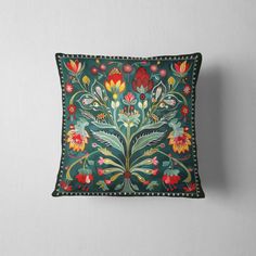 an embroidered pillow with flowers and leaves on the front, sitting against a white wall