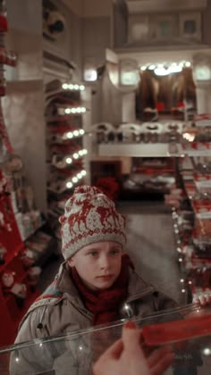 a young boy in a hat and scarf is looking through a display case at christmas decorations