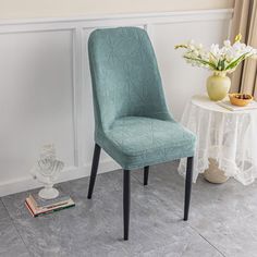 a blue chair next to a white table with flowers on it and a book near by