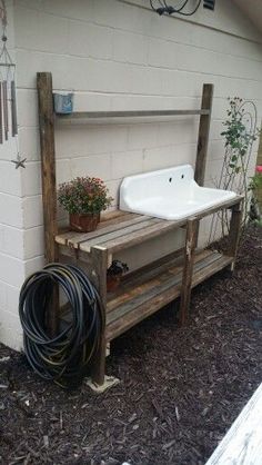 a sink sitting on top of a wooden bench next to a white brick wall and flower pot