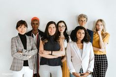 a group of women standing next to each other in front of a white wall with their arms crossed